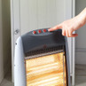 Grey electric halogen heater with lit heating element, power button pressed by hand