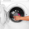 Hand placing grey and pink slippers into a washing machine