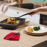 Non-stick roasting tray with cooked chicken and vegetables, hand serving to dinner plate