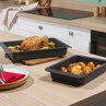 Two grey roasting trays with roast chicken and potatoes on a kitchen worktop.