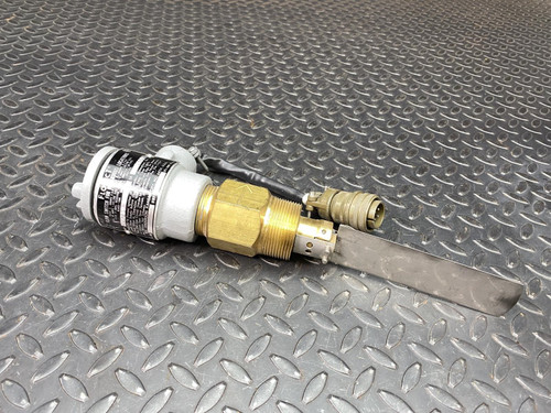 Flotect V42DU Flow Switch designed for hazardous locations, featuring a light gray cylindrical housing with a black label displaying specifications and certifications. A robust brass threaded fitting connects the main body to a flat, metallic paddle sensor, which appears to be stainless steel, used for detecting liquid or gas flow. An attached black electrical cable with a multipin militarystyle circular connector extends from the brass section, indicating its electrical interface. The durable industrial flow sensor is displayed on a dark gray diamond plate background, emphasizing its rugged construction suitable for explosionproof and demanding process control environments.