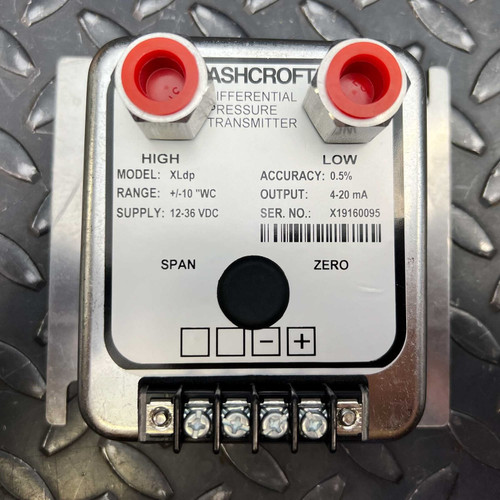 Ashcroft XLdp Differential Pressure Transmitter, a precise industrial sensor for HVAC and process control, featuring a silver metallic enclosure and a detailed white data label. Visible specifications include Model: XLdp, Range: /10 "WC for accurate differential pressure measurement, Supply: 1236 VDC, Accuracy: 0.5%, and a standard 420 mA output. The unit has two redcapped pressure ports labeled HIGH and LOW, a prominent black zero calibration button, and a terminal strip with five silver screw connections at the bottom for electrical integration. The serial number X19160095 is also clearly visible, all presented on a textured diamond plate metal background.