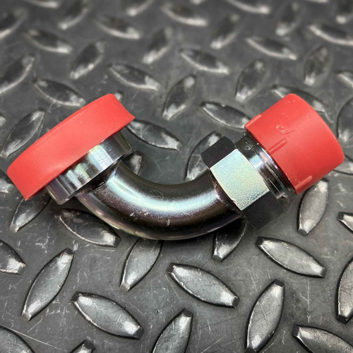 A single Eaton 90 degree split flange adapter 69012, a silver metallic hydraulic elbow fitting with a shiny, reflective surface, featuring a hexagonal nut and bright red plastic protective caps on both ends. This durable industrial hose adapter is shown horizontally against a dark gray diamond plate metal background.