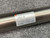 Detailed closeup shot of an SMC CM2E32200Z pneumatic air cylinder, featuring its silvertoned, brushed metallic body. A white label prominently displays the model CM2E32200, the SMC logo, MAX. PRESS: 145 PSI (1.00 MPa), and 'MADE IN USA'. This industrial doubleacting actuator, with a 32mm bore and 200mm stroke, is presented from an overhead angle on a textured dark gray surface, highlighting its robust design and specifications for automation systems.