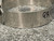 A focused shot of the side of a Clampco 2.5" stainless T-bolt clamp, showing the embossed product details along the band. Visible text reads part numbers and specifications, with "QA 172" written in marker, indicating a quality inspection from Obtainium Science and Surplus.