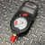 Black plastic body with light surface scuffs; analog gauge reads PSI X 100, USE NO OIL, scale to 40; red ALARM button; LCD unpowered; red port cap fitted.