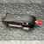 Black plastic housing with yellow button on left end, red-capped port on right, two adhesive labels partially legible on underside. Light scuffs on upper shell.