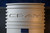 Close-up of the logo on a Cray supercomputer's central column, showcasing the embossed 'CRAY' brand name in a sleek, modern design. The logo is on a textured white surface with decorative horizontal bands and vent-like cuts, set against a dark mesh background.