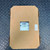 Sealed cardboard packaging with a small cutout revealing the Carrier OPNMPCXP MPC Open XP Automation Controller Module for HVAC from Obtainium Science and Surplus inside, placed on a textured black surface.