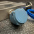 Side view of the Micro Motion Coriolis flow meter from Obtainium Science and Surplus, highlighting the blue sensor with a smooth round casing and the attached blue cable. The device rests on a textured diamond-pattern metal surface.