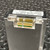 A closeup, angled view of a Matheson 82720412 Mass Flow Transducer, a metallic silver rectangular device for 100 SCCM air flow measurement. The product label is prominently visible on top, displaying "MODEL 82720412", "RANGE @0C 100 SCCM", "GAS AIR", and "PSIG INLET (30)". Within a top recess, two sets of goldplated electrical pins on green circuit boards are clearly shown, indicating its electronic nature. This industrial gas flow sensor, used for precise air flow control, rests on a dark, textured metal background.