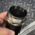 Closeup image of a Metal Work Pneumatic 9650803 Upper Cover for a 3/4 inch Regulator or Filter Regulator unit, held by a hand against a dark, textured metal background. The silver metallic cover features prominent threading and a hexagonal nut base, with a recessed black plastic cap visible on top. A small central indentation is present on the black cap. A ruler from Obtainium Science is partially visible, providing scale for this essential pneumatic air preparation component.