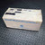A light brown, slightly worn cardboard box containing a Bodine Gearmotor 42A4BEPME4, featuring 115VDC, 21 RPM, and a 120:1 ratio. The box is printed with "Small Motors/Gearmotors" in blue lettering, alongside the Bodine Electric Company logo and address. Handwritten text, including "Tag" and obscured details, is visible on the top surface of this industrial electric motor part's packaging, which rests on a black, textured diamond plate background.