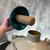 Teal plastic lid with cylindrical cork stopper held above the dewar neck; cursive marking visible on neck; cream painted exterior with light wear.