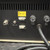 Rear view of an SIS CryoTrap Controller 951 for CO2 from Scientific Instrument Services, featuring a dark gray panel with various inputs and controls. On the left are silver threaded fittings for CO2 In and CO2 Out. In the center, there is a yellow Ktype thermocouple connector labeled "K CHROMEL  ALUMEL ", above a white 4pin connector for "CryoTrap" and a white 3pin connector for "Remote Start". To the right, two black fuse holders are visible, labeled "Heater Fuse" and "Main Fuse". A thick black power cord exits from the bottom right of the scientific instrument. The top of the unit shows black vertical ventilation slots. This image highlights the rear connections and power input for this laboratory CO2 controller.