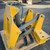 Yellow-painted steel frame with hydraulic cylinder, hoses, and fittings intact. Five black serrated shanks visible. Minor surface scuffs on cylinder rod.