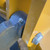 Yellow-painted steel frame with light scuffing and whitish surface marks; dark blue-grey cast iron wheel hub shows surface rust patches and a grease zerk fitting.