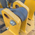 Yellow-painted steel frame with gray roller and bolt showing surface rust bleed at seams; minor paint chips on left cheek plate.