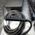 Detailed view of the black magnetic Surface Connect charging cable from an unused Microsoft Surface 65W Power Supply with USB, Model 1706. The closeup focuses on the connector, clearly showing its two sets of three gold pins, characteristic of a Surface laptop charger. The robust black power cable is neatly coiled in the background, suggesting a new or pristine condition for this essential AC adapter replacement for Surface devices.