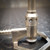 A closeup, sharpfocus image of a Classic Pittsburgh Universal Bunsen Burner, Model 1348 by Eimer and Amend. The durable, brushed silvertoned metal laboratory gas burner features an adjustable air collar with visible vents, a gas intake hose barb on the left, and a gas adjustment needle valve at the base. Embossed text "PITTSBURGH" and "UNIVERSAL" is visible on the base, highlighting this essential science equipment for chemistry labs.
