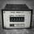 front view of "A black ECCI MBRM-215 input calibrator module on a textured gray surface, featuring a front label with white text specifying model details and serial number '865343.'