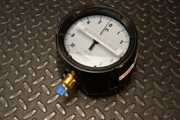 Ashcroft pressure gauge with a black casing and a 4.5-inch white face displaying a dual scale ranging from 10 in. Hg vacuum to 5 PSI, featuring a brass socket connection with a blue protective cap.