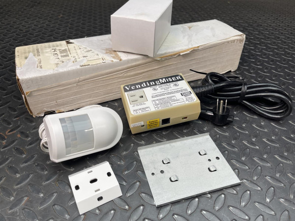 Vending Miser unit, motion sensor, power cord, mounting bracket, and outlet plate on a dark surface.