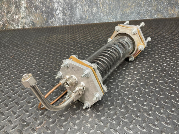 Custom-made vacuum/pressure chamber with an internal heat-exchange coil from Obtainium Science and Surplus, resting on a textured, black metal surface. The chamber has a cylindrical design with metal end plates and visible connecting tubes.