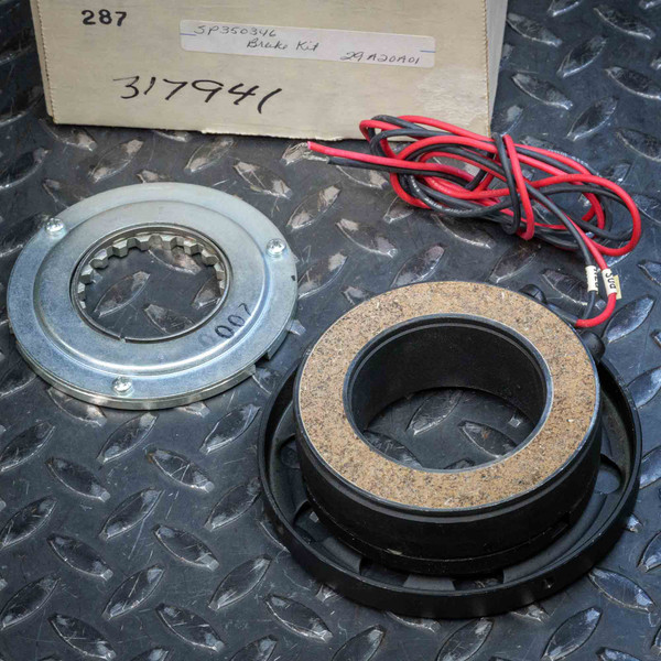 Warner Electric 5370-631-007 Clutch Brake Magnet and Armature from Obtainium Science and Surplus, showing both main components with red and black wires beside a labeled cardboard box, placed on a textured metal surface.