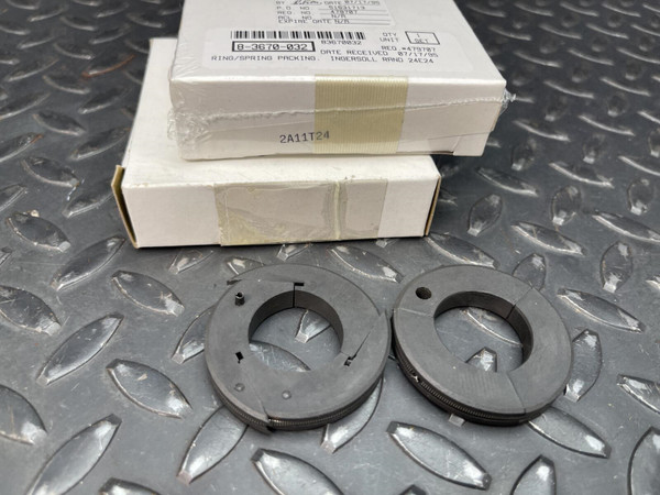 Two Ingersoll-Rand 2A11T24 packing rings with springs and their factory packaging on a metal surface.