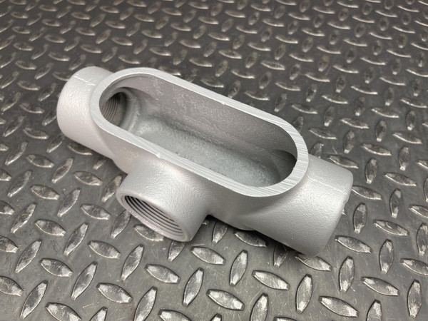 T conduit body from Obtainium Science and Surplus displayed on a metal surface, showing its oval-shaped opening and three threaded ports.