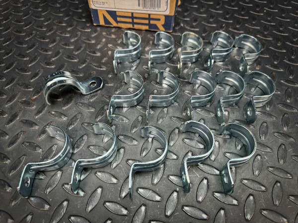 Sixteen Neer 1904 1-1/4 inch EMT conduit straps, zinc-plated steel, on a diamond plate surface.