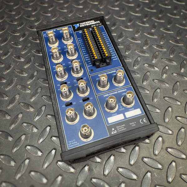 National Instruments BNC-2110 terminal block from Obtainium Science and Surplus shown on a textured metal surface, featuring multiple input and output connectors.