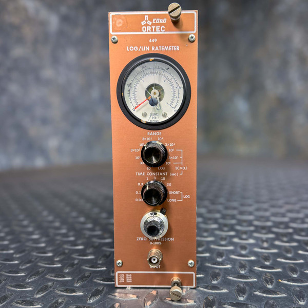 Front view of an Ortec 449 LOG/LIN Ratemeter, featuring a large analog meter at the top displaying counts per second. Below the meter are various control knobs for adjusting range, time constant, and zero suppression. The device is housed in a copper-colored panel, and is designed for use in nuclear spectroscopy. This image was taken on a metal textured surface.
