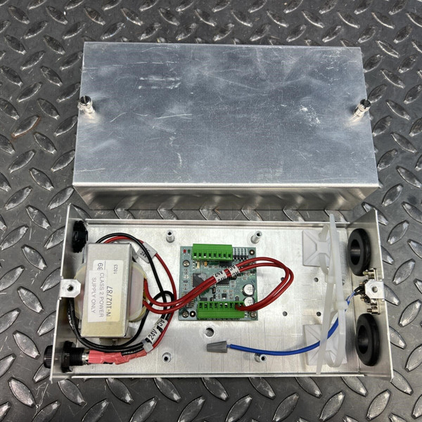 A Johnson Controls Metasys Universal Valve Module UVM1000 from Obtainium Science and Surplus with its metal casing open, showing internal wiring, circuit board, and components on a diamond plate metal surface.