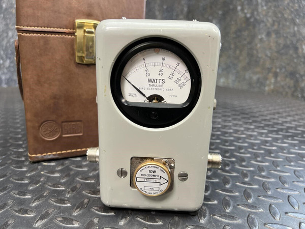 A Bird 43 wattmeter from Obtainium Science and Surplus on a textured metal surface. The wattmeter features a round analog display marked with watts, and a control knob below.
