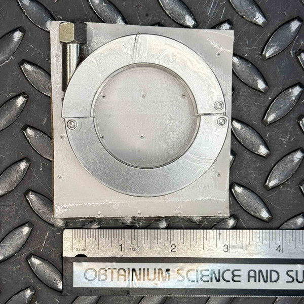 Detailed product image of an ANCORP QF40CLMPSS KF40 Vacuum Clamp, crafted from durable 304 stainless steel, resting on a dark industrial diamond plate surface. The silver metallic clamp features a split circular design for connecting KF40 vacuum flanges, with two small visible screws securing one hinge point and a larger hexagonal bolt on the left for tightening the connection. A silver ruler at the bottom, showing measurements in inches, indicates the clamp's approximate width of 3.5 inches, ideal for high vacuum systems and scientific applications.