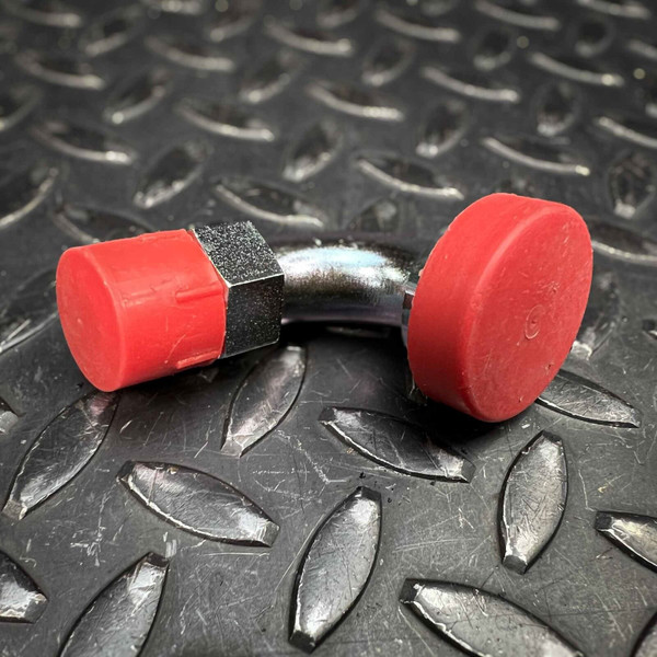 Eaton 90 degree split flange adapter 69008, a gleaming metallic hydraulic elbow fitting with a chrome finish, shown with vibrant red protective caps covering both ends. The durable industrial hose adapter features a distinct hexagonal nut section, set against a dark gray, textured diamond plate metal background, highlighting its robust design. This detailed image showcases one unit from the Eaton 69008 pack of 4, emphasizing its quality and application.