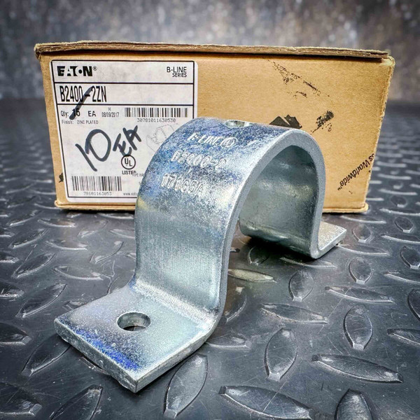 Unused, heavy-duty, zinc-plated Eaton B2400-2ZN strut pipe clamp on a metal floor with its product box.