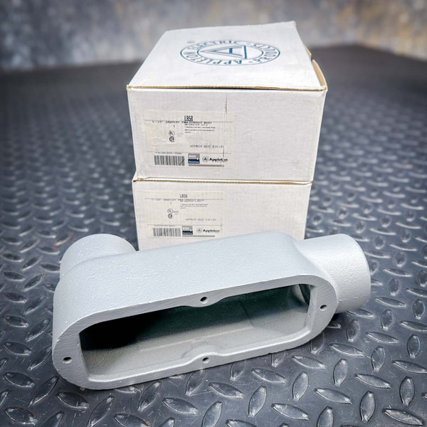 Unused Appleton 1-1/2" LB58 gray cast metal conduit body displayed open, with two product boxes stacked on diamond plate.