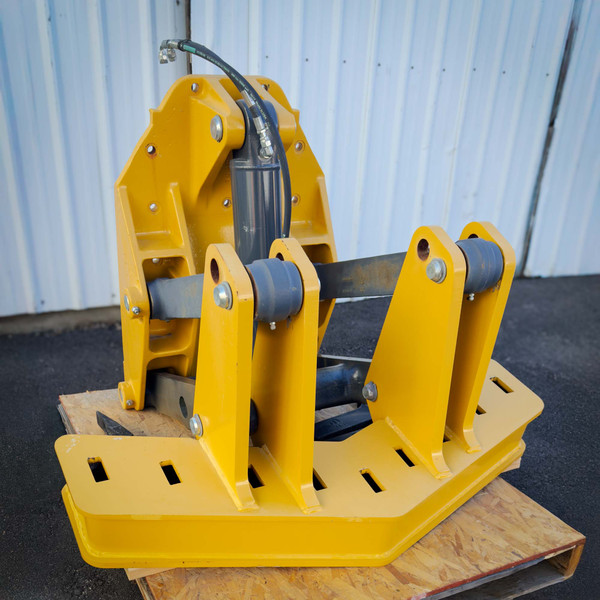 A yellow Front Mount Scarifier for John Deere Motor Graders from Obtainium Science and Surplus, resting on a wooden pallet against a corrugated metal wall.