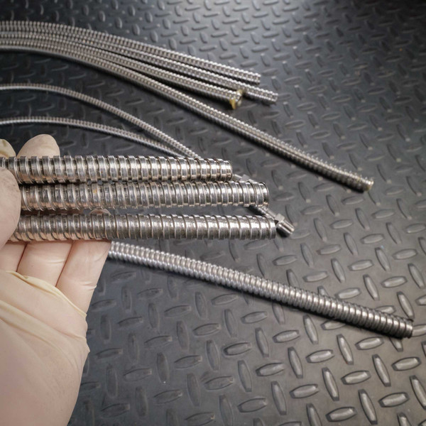Multiple flexible SS conduit wire guides fanned out; interlocked spiral wrap intact, minor surface patina, bare wire tips visible at ends.