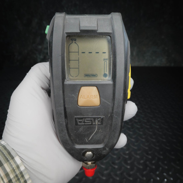 LCD active showing cylinder graphic, psi bar, and dashed alarm indicators. ALARM button intact. Light surface scuffs on housing. Red-capped inlet fitting present.