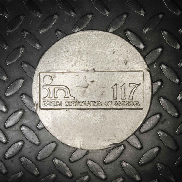 Embossed "in 117 / INDIUM CORPORATION OF AMERICA" on matte silver disc face; light surface scuffs and minor soiling visible across face.