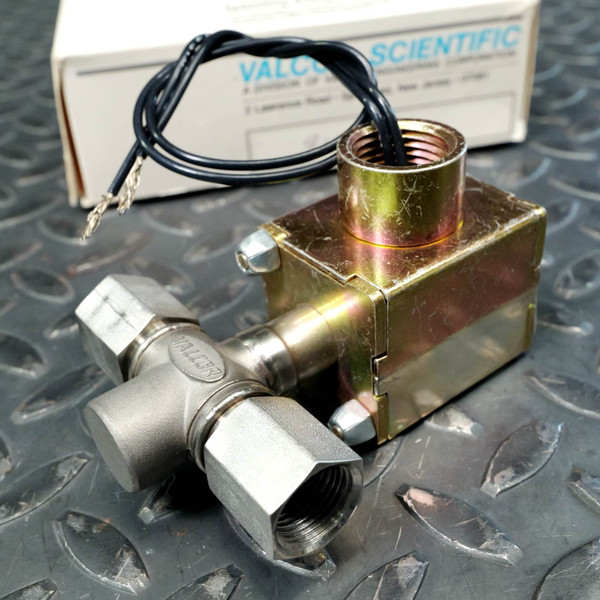 Stainless valve body with VALCOR embossed on body, zinc-plated solenoid housing, two bare lead wires exiting top, acorn-nut fittings visible.