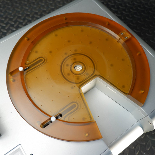 Top view of the orange circular platform of the ProTec electrostatic wafer handling chuck racket, with a cutout section and small white pegs visible.