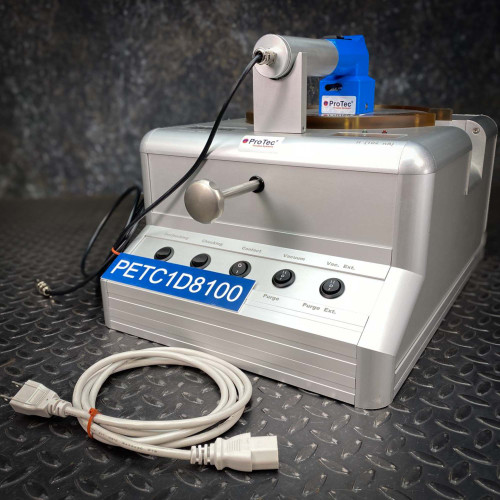 Side angle of a ProTec electrostatic wafer handling chuck racket, showing its control panel and a coiled cable, with an additional white power cord placed in front of the device on a metal surface.