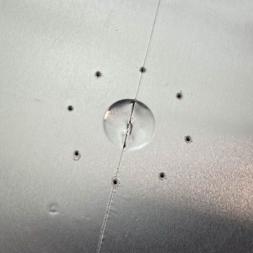 Close-up of the metal surface of a ProTec electrostatic wafer handling chuck racket from Obtainium Science Surplus, highlighting small drilled holes and a central indentation.
