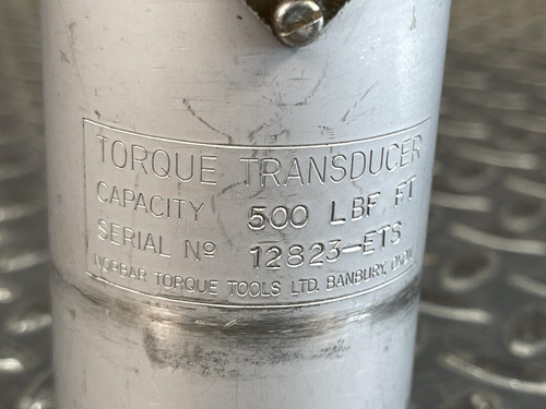 Detailed view of the engraved label on the Norbar Torque Transducer. It reads “500 LBF·FT” along with serial details. The surrounding silver finish shows slight wear, set against a textured metal surface.