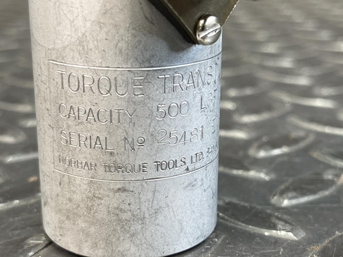 Close-up of the Norbar Torque Transducer 500 LBF·IN label, with engraved specifications on the cylindrical metal body, highlighting measurement and model details. The device rests on a textured metal background.
